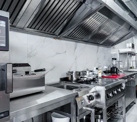 ¿Cómo elegir muebles de acero inoxidable? ¡Descubre sus beneficios! 3 Fila de electrodomésticos hechos con acero inoxidable en una cocina industrial, se encuentran de lado izquierdo y tienen una campana de cocina sobre ellos