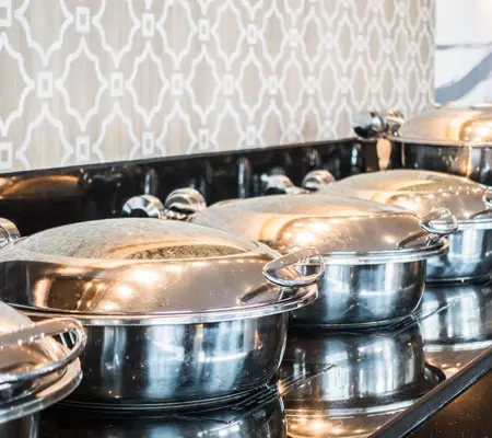 ¿Cómo elegir muebles de acero inoxidable? ¡Descubre sus beneficios! 4 Ollas de acero inoxidable con tapa en fila, sobre una estufa industrial