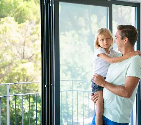 Perfiles de aluminio para ventanas: Usos y ventajas. ¡Descubre consejos para una fácil instalación! 2 Hombre que carga en brazos a una niña mirando hacia balcón exterior de una ventana deslizante hecha con perfiles de aluminio
