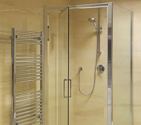 Puertas de Aluminio ¡La mejor opción para el hogar! 3 Vista frontal de una puerta y vidrio para baño que cerca el área destinada a la regadera, a la izquierda hay una estructura metálica para colocar las toallas