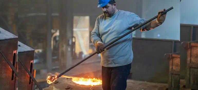 La importancia del punto de fusión del acero inoxidable 1 Trabajador de una fundidora revisando con una varilla una muestra de acero inoxidable en su punto de fusión, al fondo se ve la maquinaria de la fábrica fundidora
