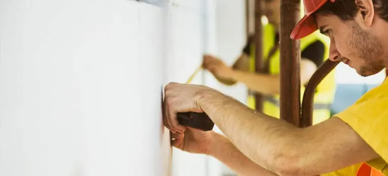 La cinta métrica ¿para qué sirve? 4 Trabajadores con casco naranja y playera amarilla midiendo longitudes sobre una pared blanca